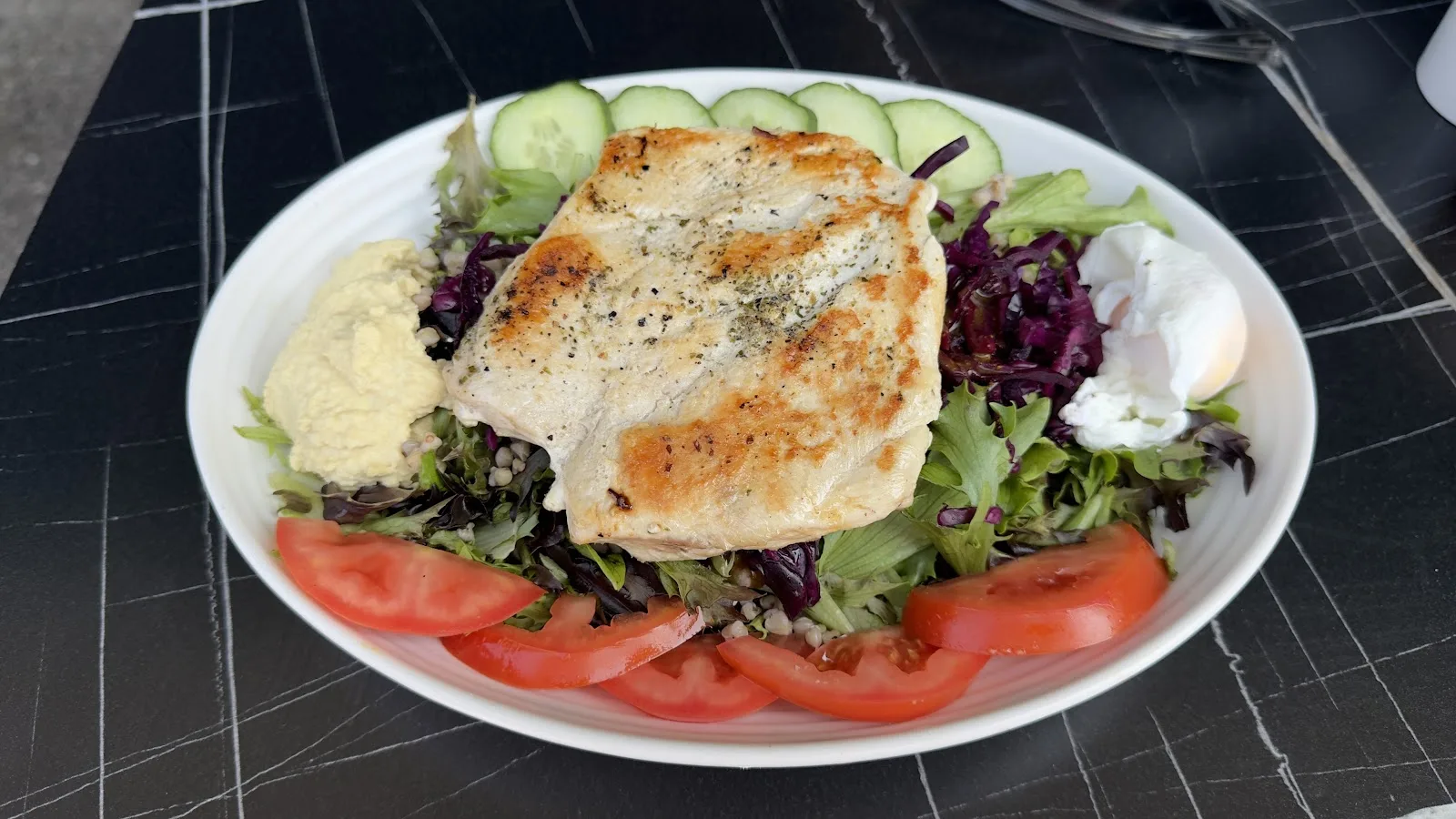 Grilled chicken with hummus, red cabbage, tomato, cucumber and a poached egg on a salad plate at Isla Bay