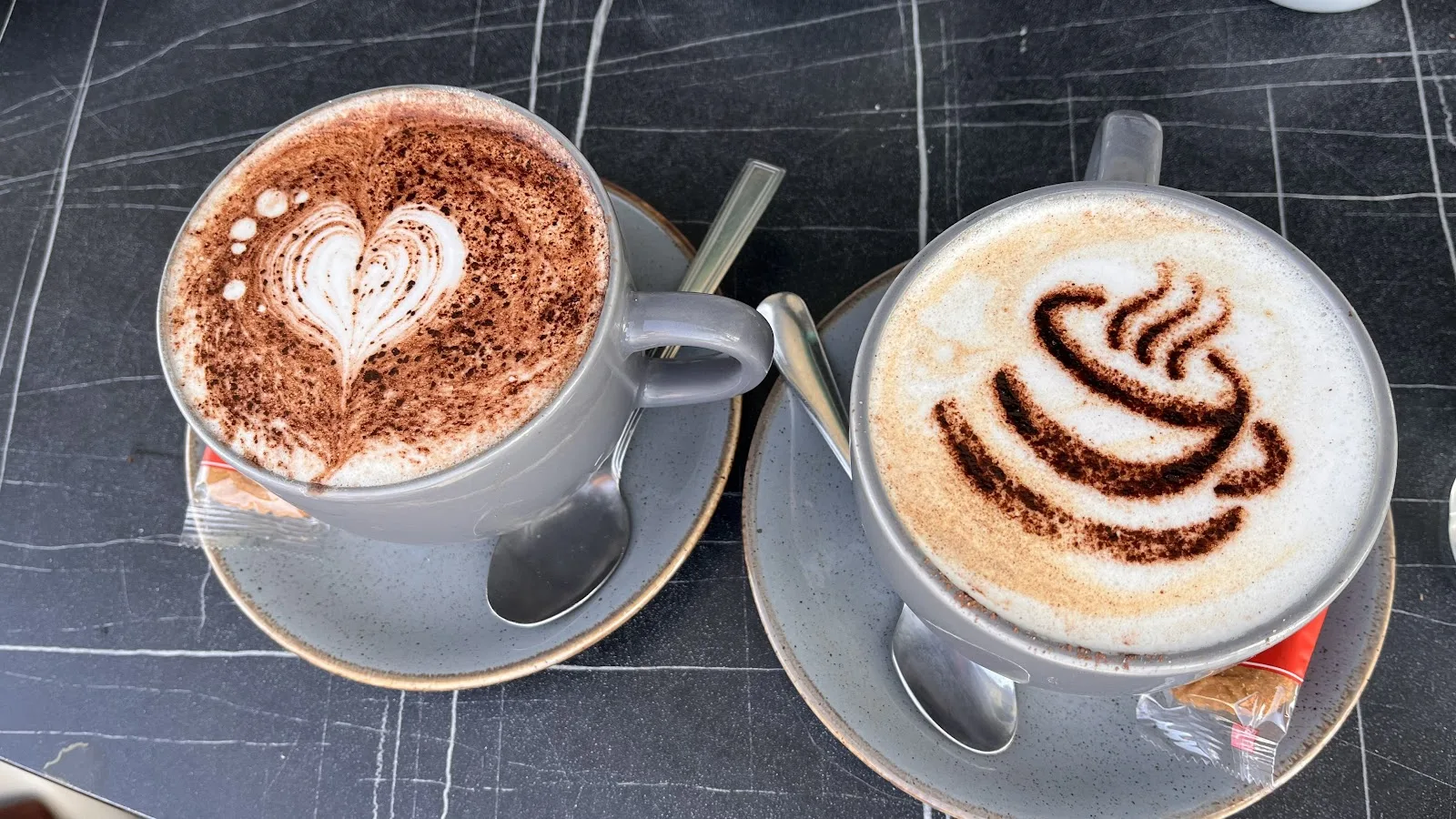 Two cappuccinos with latte art and cocoa dusting on a marble table at Isla Bay