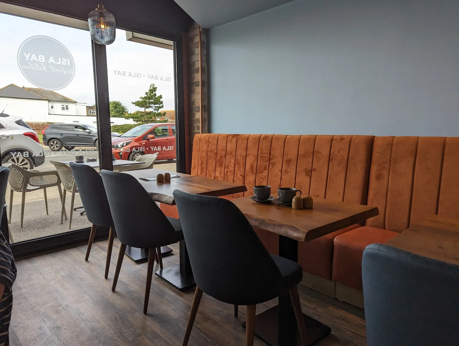 Inside Isla Bay: rust velvet banquettes, live-edge wooden tables and big windows onto the seafront